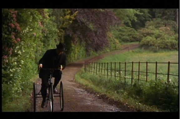 man in black rides tricycle; Simon Callow as Mr. Beebe in A Room With A View