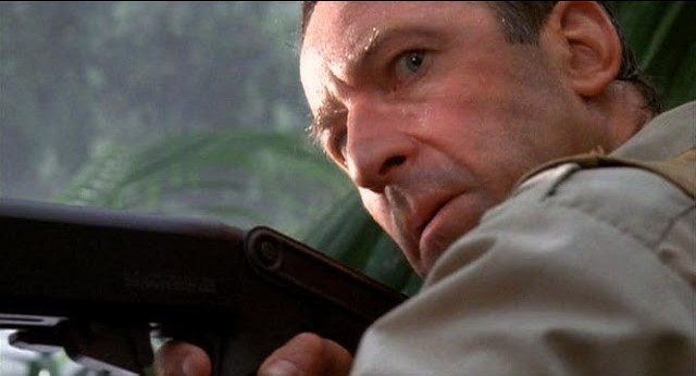 white man looks suspiciously over a gun; still from Jurassic Park
