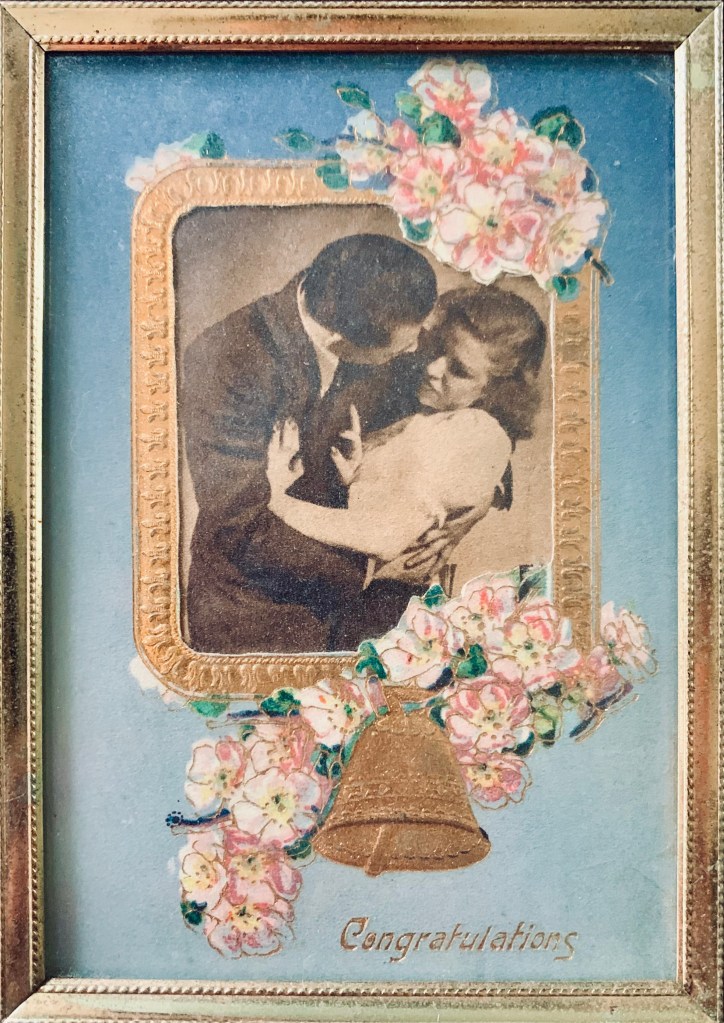 a woman resists a man's romantic attempt while ironically framed in a wedding bells postcard