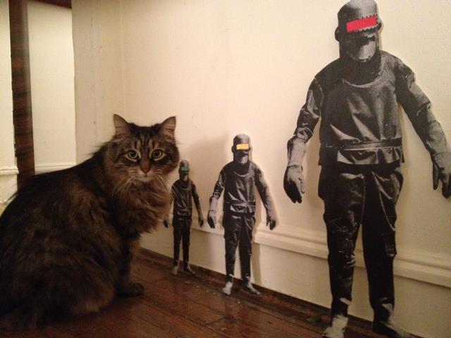 longhaired brown cat sits next to three oversized cutouts of spacemen