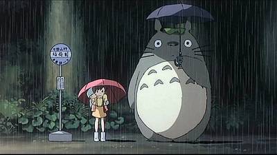 small girl with umbrella in the rain stands next to giant forest spirit in Miyazaki's Totoro