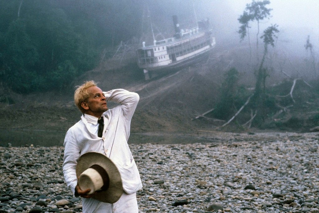 white man in a white suit looks concerned as he stands in front of a riverboat stuck on the side of a mountain; Klaus Kinski in Werner Herzog's Fitzcarraldo